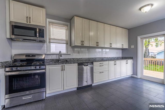 kitchen featuring decorative backsplash, stainless steel appliances, white cabinets, and a sink