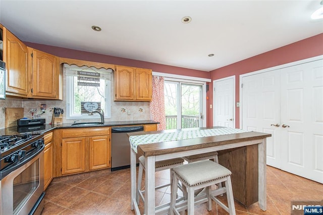 kitchen with backsplash, dark countertops, stainless steel appliances, and a sink