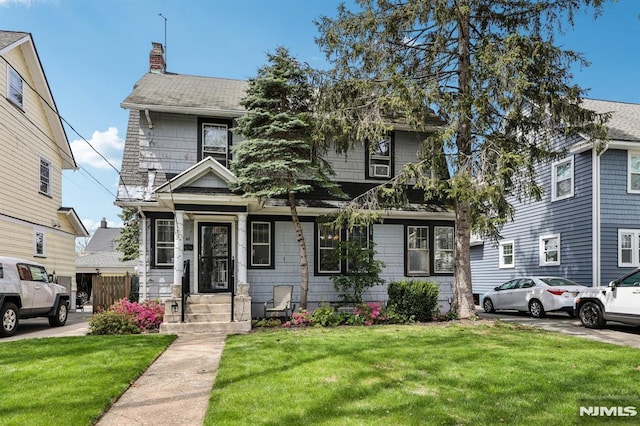 view of front facade featuring a shingled roof, a chimney, and a front lawn