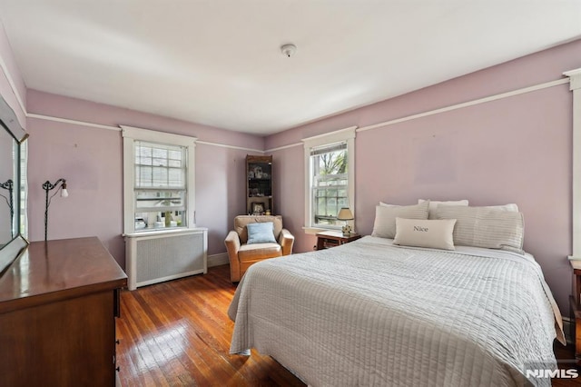 bedroom with baseboards, multiple windows, radiator heating unit, and hardwood / wood-style floors