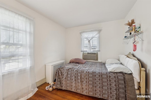 bedroom with cooling unit, a baseboard heating unit, and wood finished floors