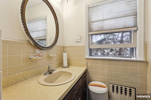 half bath with tile walls, wainscoting, vanity, toilet, and radiator