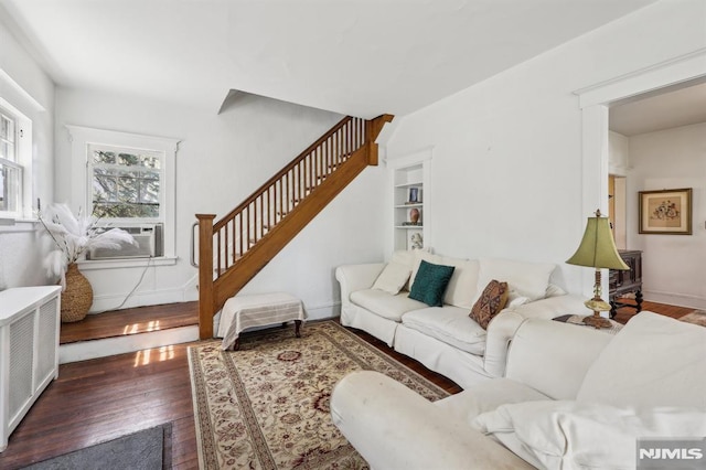 living room featuring wood finished floors, baseboards, cooling unit, radiator, and stairs