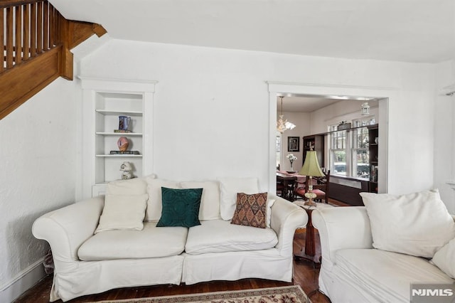 living room with wood finished floors, a chandelier, and built in shelves