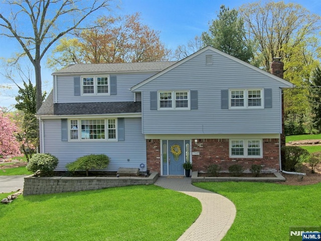 split level home with a chimney, brick siding, a front lawn, and roof with shingles