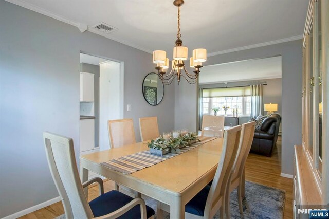 dining room with an inviting chandelier, wood finished floors, crown molding, and visible vents