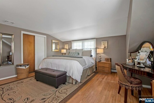 bedroom featuring lofted ceiling, visible vents, light wood-style flooring, and baseboard heating