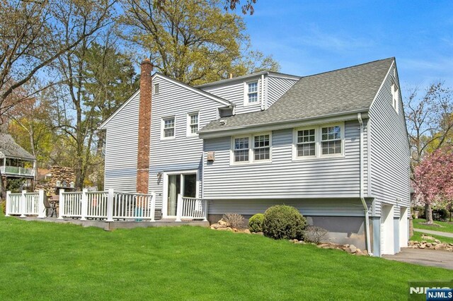 rear view of property featuring a deck, a chimney, an attached garage, and a lawn