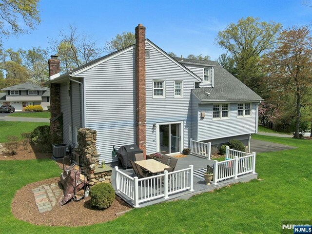 rear view of property with a chimney, central air condition unit, a shingled roof, a yard, and a wooden deck