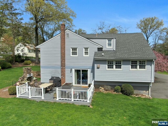 back of house with a chimney, a patio area, a shingled roof, and a lawn