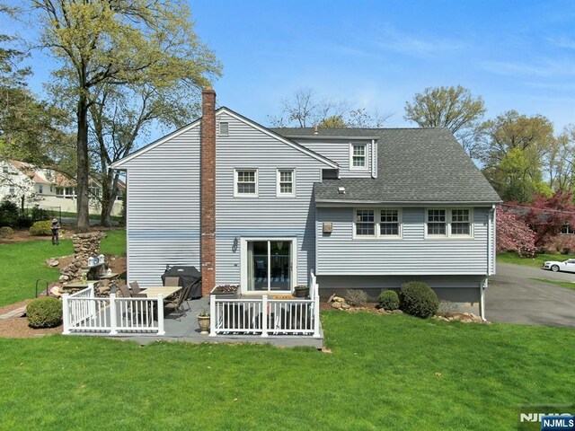 rear view of house featuring a lawn, a patio, a shingled roof, and a chimney