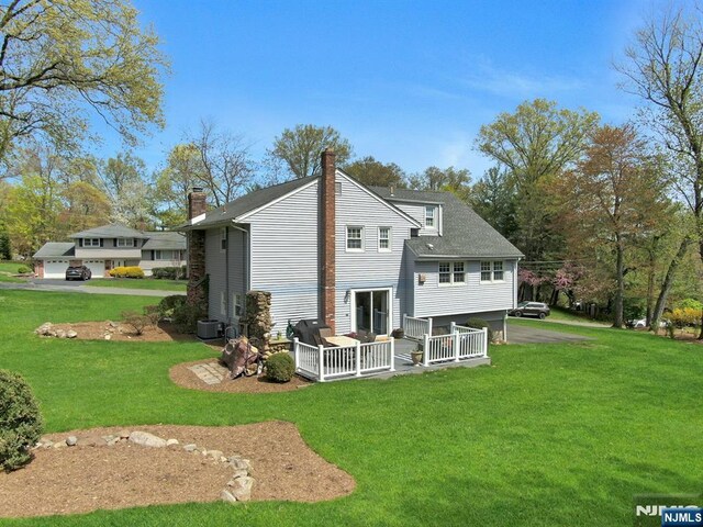 back of house with a wooden deck, a lawn, central AC, and a chimney