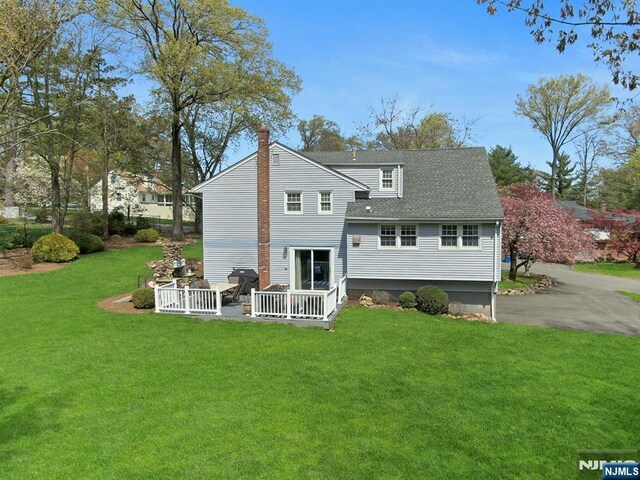 rear view of property with a chimney, a shingled roof, and a lawn