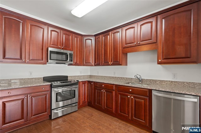 kitchen featuring stainless steel appliances, a sink, light wood-style flooring, and light stone countertops