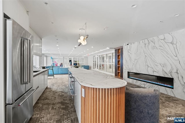 kitchen with high end fridge, modern cabinets, open floor plan, a high end fireplace, and recessed lighting