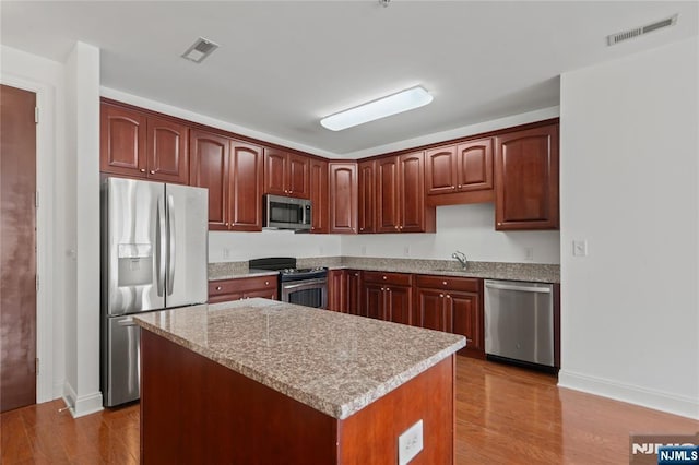 kitchen with appliances with stainless steel finishes, wood finished floors, baseboards, a sink, and a kitchen island