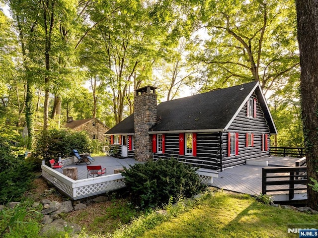 back of property featuring log exterior, a chimney, and a deck