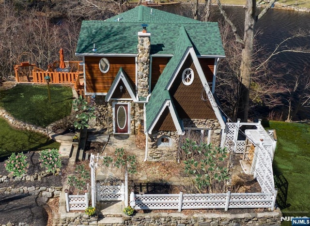 view of front facade featuring fence, stone siding, a shingled roof, and a front yard