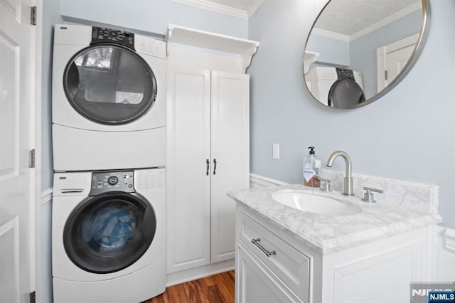 clothes washing area with a sink, stacked washer / dryer, dark wood finished floors, and crown molding