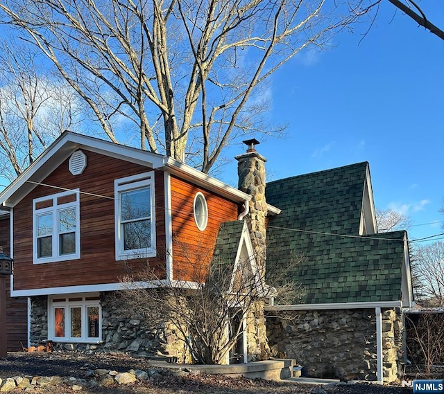 view of side of property with stone siding, a chimney, and a shingled roof