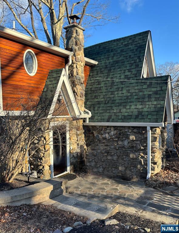 view of front of home with a chimney, roof with shingles, and stone siding