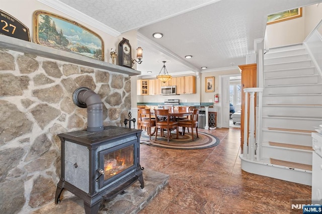 living area with a textured ceiling, a wood stove, stairs, and ornamental molding