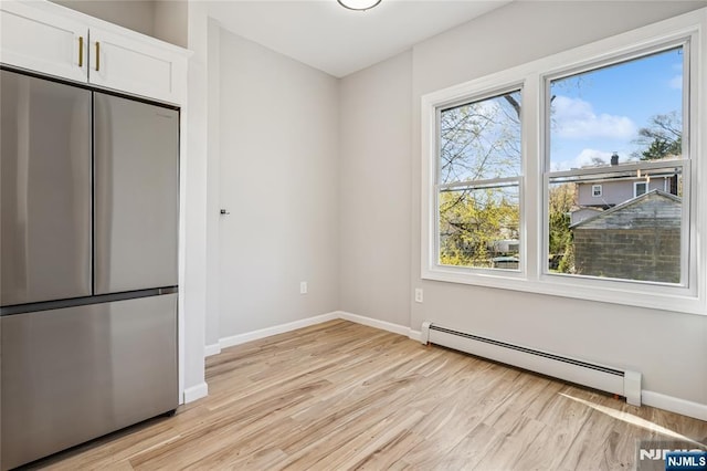 unfurnished dining area with a baseboard heating unit, baseboards, and light wood-type flooring