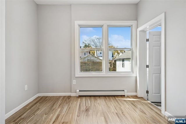 spare room with a baseboard heating unit, baseboards, and light wood-style flooring