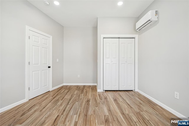 unfurnished bedroom with a closet, a wall unit AC, light wood finished floors, baseboards, and recessed lighting