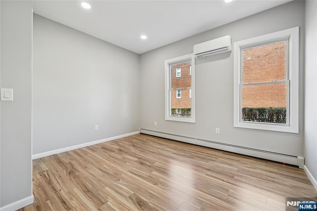 spare room featuring a baseboard heating unit, an AC wall unit, baseboards, and light wood-type flooring