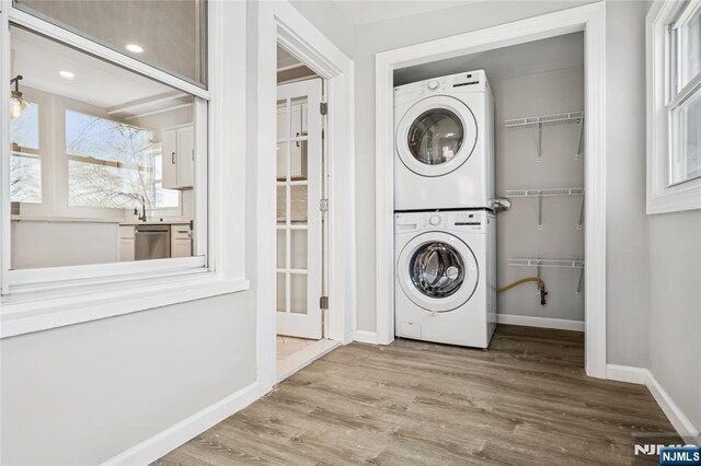 washroom with stacked washer and dryer, wood finished floors, baseboards, and laundry area