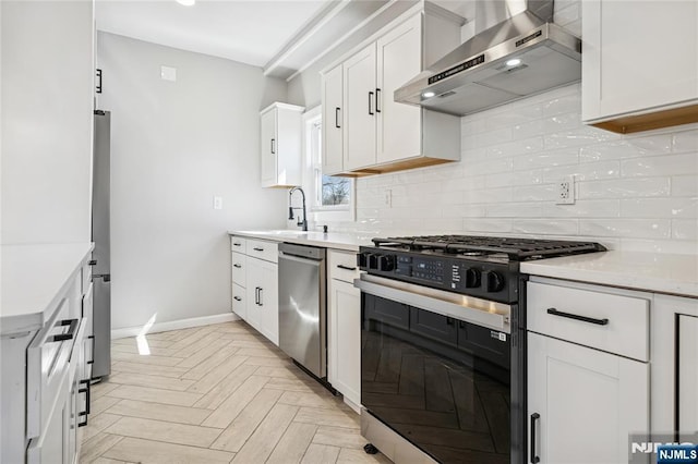 kitchen with backsplash, light countertops, wall chimney range hood, a sink, and appliances with stainless steel finishes