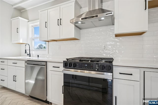 kitchen featuring light countertops, stainless steel dishwasher, gas stove, and wall chimney range hood