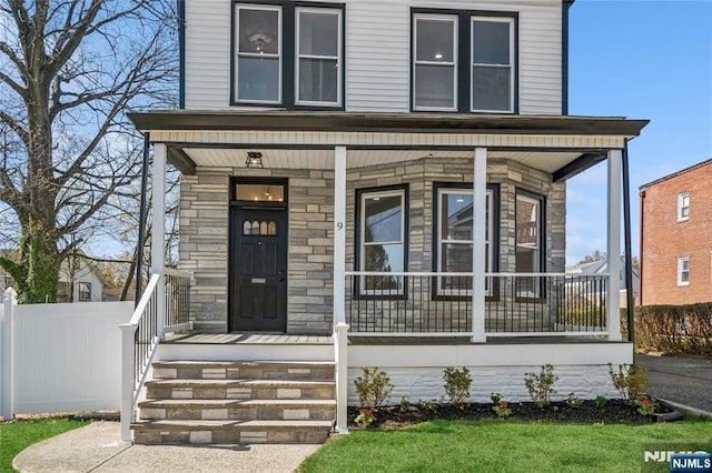 view of front of property with a porch, stone siding, and fence