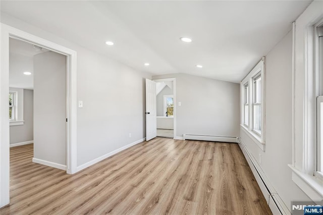 spare room featuring a baseboard heating unit, light wood-style floors, and a healthy amount of sunlight