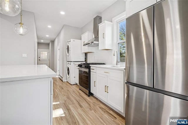 kitchen with a sink, light wood-style floors, stacked washer and clothes dryer, wall chimney range hood, and appliances with stainless steel finishes