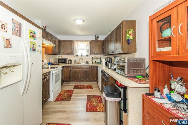 kitchen featuring under cabinet range hood, light countertops, a sink, white appliances, and light wood-type flooring
