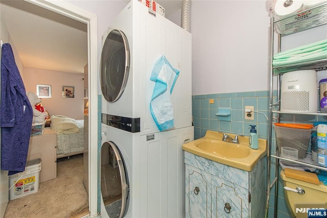 bathroom featuring connected bathroom, wainscoting, vanity, stacked washer / dryer, and tile walls