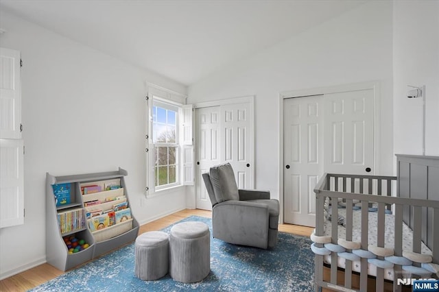 bedroom featuring baseboards, vaulted ceiling, wood finished floors, and two closets