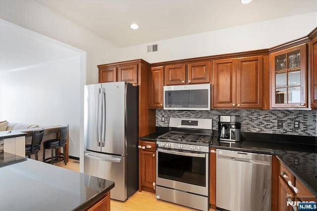 kitchen featuring visible vents, backsplash, glass insert cabinets, brown cabinets, and appliances with stainless steel finishes