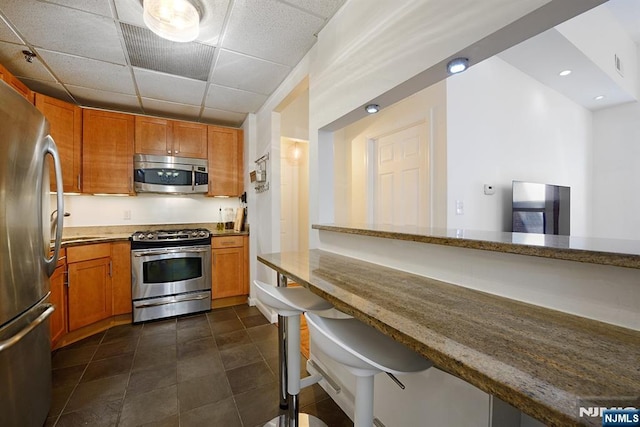 kitchen with stainless steel appliances, light stone countertops, brown cabinetry, and a breakfast bar area