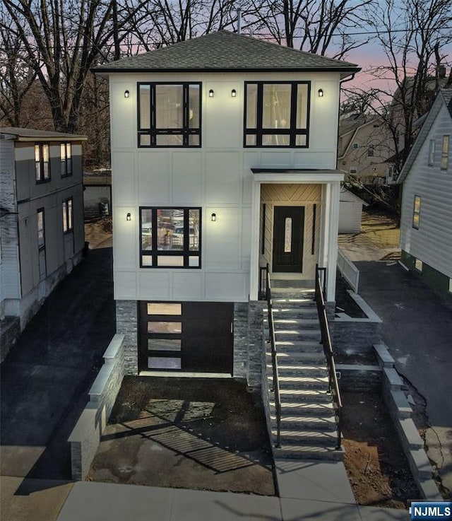 view of front facade featuring roof with shingles and stairs
