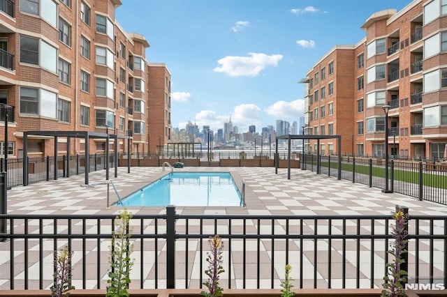 community pool featuring a patio, fence, and a city view