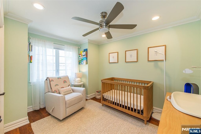 bedroom with baseboards, ornamental molding, wood finished floors, and a crib