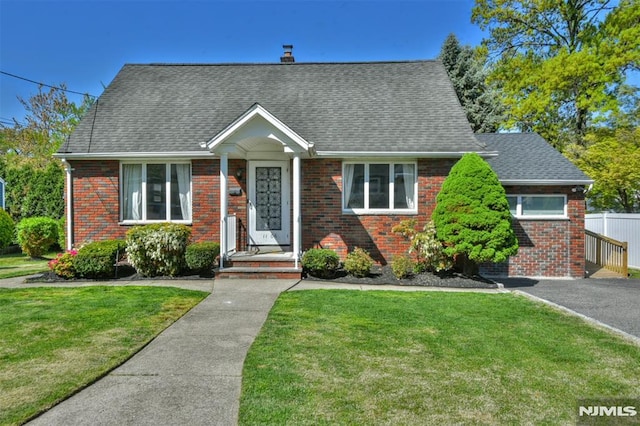 new england style home featuring brick siding, a shingled roof, a front yard, and a chimney