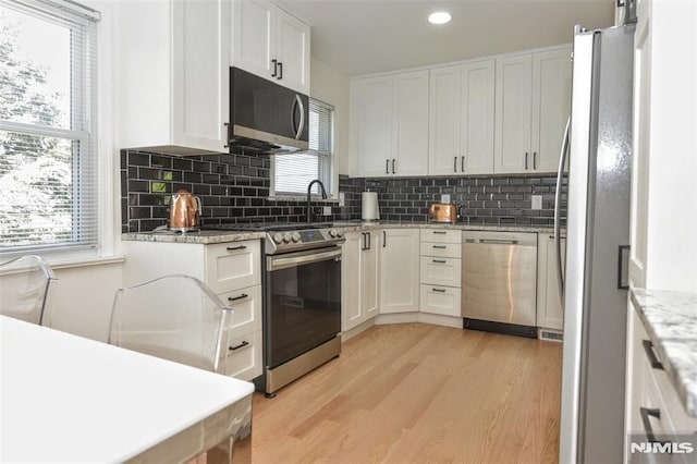 kitchen featuring appliances with stainless steel finishes, decorative backsplash, light wood-type flooring, and white cabinetry