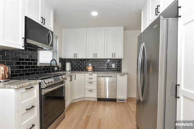 kitchen with backsplash, stainless steel appliances, white cabinetry, and light wood finished floors