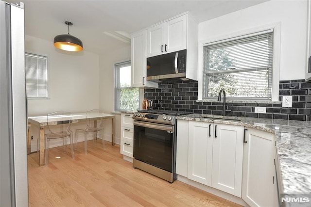 kitchen featuring light wood-style floors, white cabinetry, a sink, appliances with stainless steel finishes, and backsplash