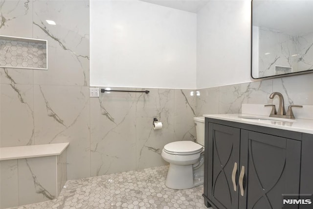 bathroom with toilet, tile walls, and vanity