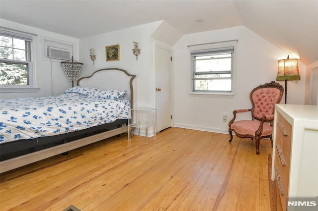 bedroom featuring baseboards, a wall unit AC, vaulted ceiling, and light wood finished floors
